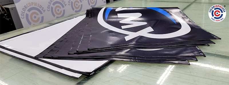 Custom vinyl banners stacked on the production table at ColorCopiesUSA - bulk banner printing order ready for finishing Stack of custom printed vinyl banners on the finishing table at ColorCopiesUSA production facility in Oakland Park Florida